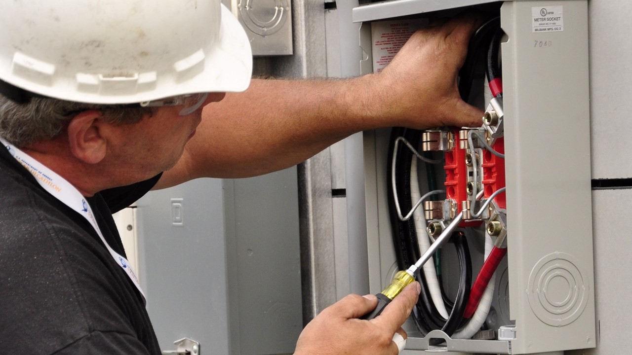 Electrician installing a residential meter socket on the exterior of a house